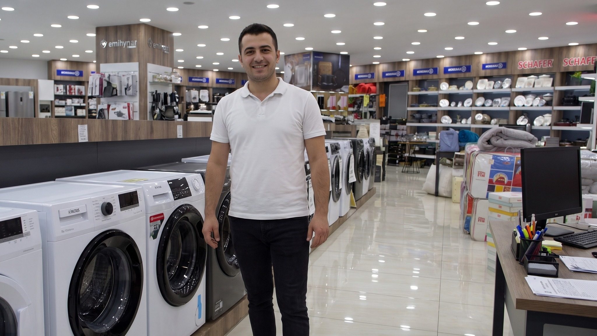 Çamaşır makinesi reyonunun önünde duran mağaza çalışanı ve yanında danışma bankosu